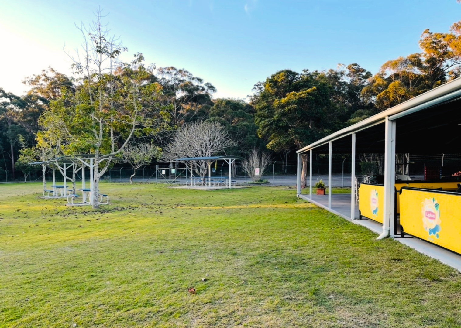 Featured is the open lawn greens with outdoor tables and chairs outside the Kiosk at Tomaree Aquatic Centre