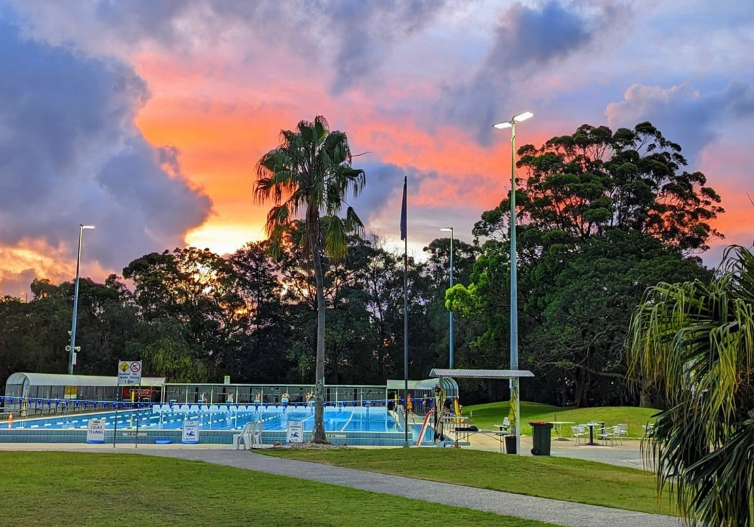 Featured is the Tomaree Aquatic Centre in the evening with a purple pink sunset. The 50m outdoor heated pool can be seen in the back.